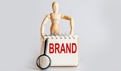 Wooden man shows with a hand to white notepad with text BRAND