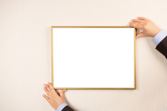 blank picture frame hanging on a beige wall. Hands hanging photo frame mockup on wall