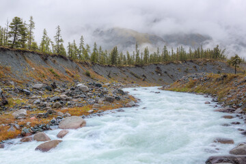 River in a mountain valley. The clouds are flying over the mountains. Mountainous terrain. Soft focus.