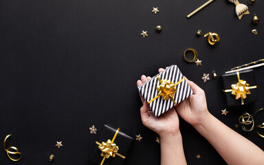 Merry christmas and new year celebration concepts with person hand holding gift box and ornament in golden color on dark background