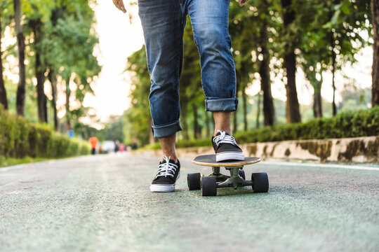 Closeup Asian man leg on surfskate or skate board in outdoor Park when sunrise time over photo blur of unrecognized people running, extream sport, healthy and exercise, fashion in covid19 concept