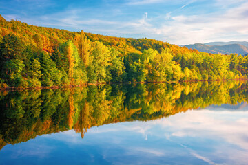 gilau lake of cluj country in evening light. beautiful landscape of romania in autumn. reflection on the calm water surface. trees in colorful foliage. sunny weather