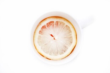 Lemon slice in a cup with black aromatic tea on a white isolated background, top view.