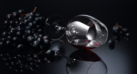 Blue grapes and wine glass with red wine on a black reflective background.
