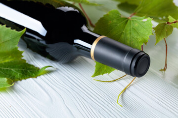 Unopened red wine bottle and vine twig on a white wooden table.