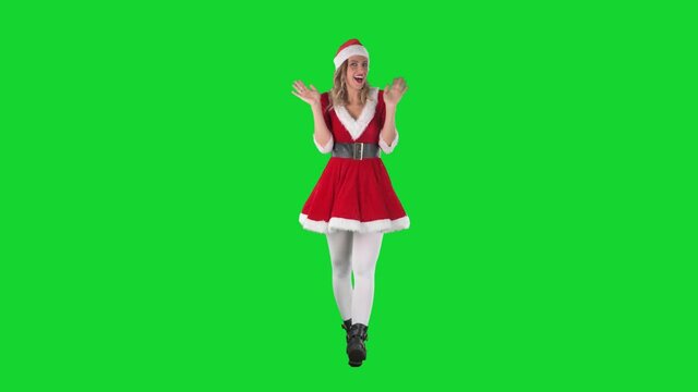 Excited cheerful girl in Santa Christmas costume walks and greet waving hand at camera. Full body length on green screen background. 