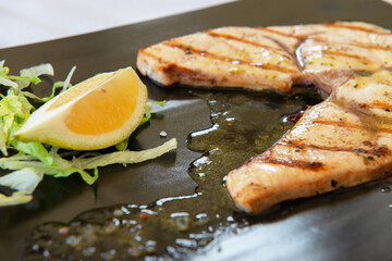 Cooked swordfish. Grilled slice of fish with lemon and salsd on plate in restaurant