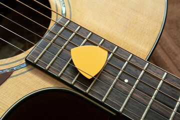 Yellow guitar pick on acoustic guitar