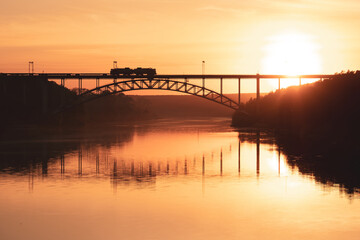 silhouette of a train on a railway bridge over the river during sunset