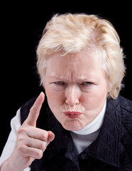Studio photo of older woman with an angry look making a warning finger gesture. Black background.