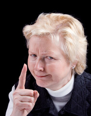 Studio photo of older woman with an angry look making a warning finger gesture. Black background.