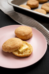 Homemade Flaky Buttermilk Biscuits on a pink plate on a black background, side view.