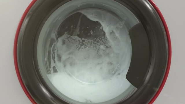 Close up view porthole of washing machine. Washing clothes process in slow motion.