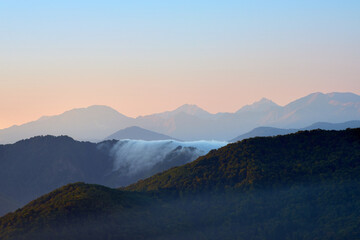 Naklejka na ściany i meble Mountain range at sunrise, fog and autumn forest