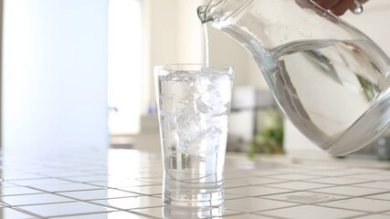 グラスに水を注ぐ、明るいキッチンで冷たいミネラルウォーターを注ぐ。