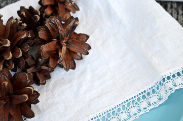 Pine cones of dark brown and golden brown color against a background of a white linen scarf with lace