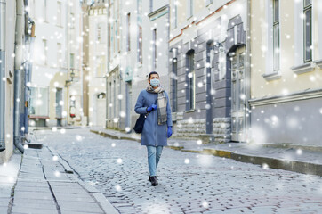 health, safety and pandemic concept - young woman wearing protective medical mask on empty street of old town in tallinn city over snow