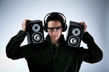 Studio photo of a dark haired young man with audio equipment, headphones and loud speakers in hands.