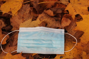 Disposable face mask lying on the street around plant leaves in autumn during Covid19 pandemic second wave.
