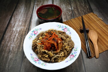 Fried and stirred noodle with egg and pork meat topping with Kimchi (Pickled mixed vegetable in Korea style) on the plate. Famous traditional menu set in Asia restaurant. 