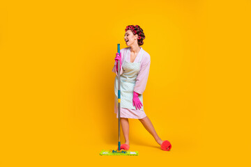 Full length body size view of cheerful funny maid singing hit using mop like mic isolated bright yellow color background