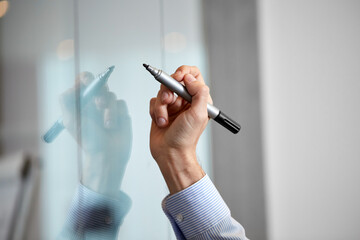 people, business and corporate concept - close up of hand with marker with sticky notes on glass wall at office