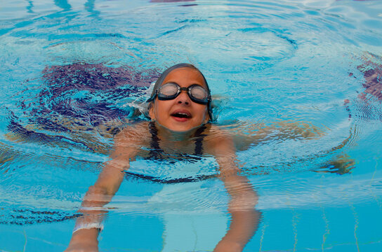 girl in swimming goggles swims in a blue pool