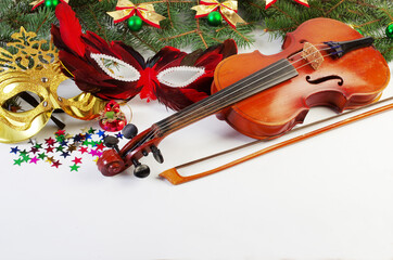 Violin, bow, carnival masks and Christmas decorations on a Christmas tree branch.