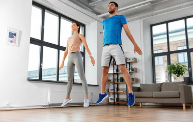 sport, fitness and healthy lifestyle concept - smiling man and woman exercising and jumping at home