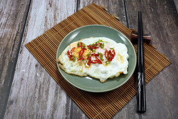 Fried fresh egg seasoning with sliced chilly and fish sauce on the plate. Famous traditional egg menu in Asia restaurant. 