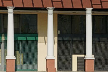 a row of white concrete columns against a gray metal mesh wall on a city street on a sunny day