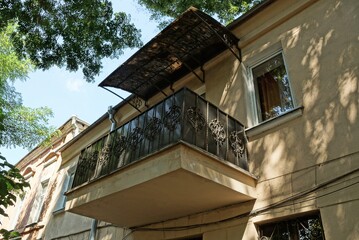 one open iron balcony with a wrought iron pattern under a black metal canopy covering on a brown wall of a house with windows on the street