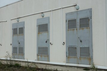 electric transformer behind a concrete wall and three iron gray closed doors on the street