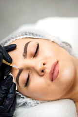 Top view of permanent makeup on eyebrows of young caucasian woman by special tattoo tool