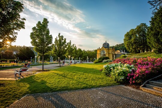 Marianske Lazne / Czech Republic - August 8 2020: View of the Maxim Gorky colonnade and singing water fountain. Colorful flowers, green lawn. Summer sunset in famous spa city with blue sky and clouds. - Powered by Adobe