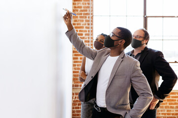 Business people wearing masks brainstorming on a whiteboard, the new normal - Powered by Adobe