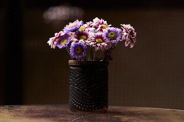 Colorful chamomile flowers in black vase on table