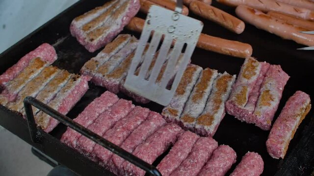 Flipping over minced meat on grill with aluminium spoon. Čevapčiči or chevapchichi.