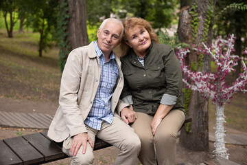 Senior elder caucasian couple together in park in spring or autumn. Wife hugging husband and smile with happiness. Beautiful love relation and care of retirement old people.