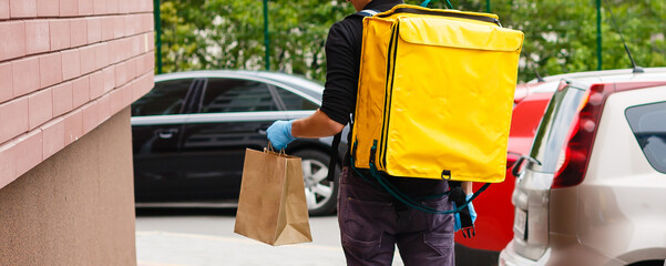 Young courier with thermo bag near the house. Food delivery service