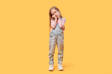 Fototapeta premium Little sad girl looks at the camera, full-length. Yellow isolated background.