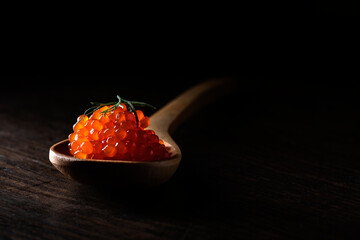 salmon caviar in a wooden spoon with dark background