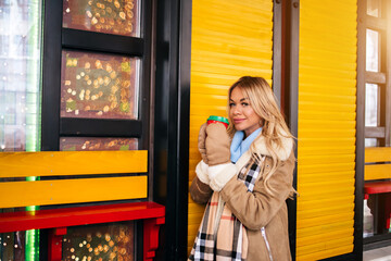 Portrait of pretty blonde girl walking in city drinking coffee