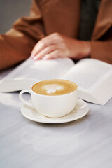 Woman reading book and drinking coffee at cafe, outdoors
