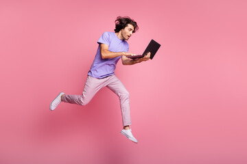 Fototapeta na wymiar Full size profile side photo of brown haired bristled guy wear purple t-shirt pink pants hold laptop jump up run isolated on pink color background