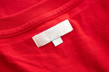 White blank clothing tag label on new red cotton shirt fabric texture background