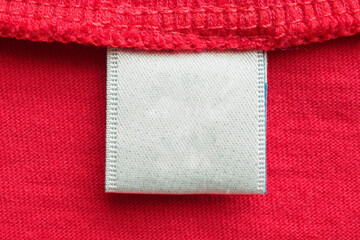 White blank laundry care clothes label on red cotton shirt background