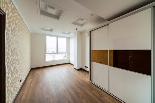 Empty room with wardrobe, window, parquet and wallpaper