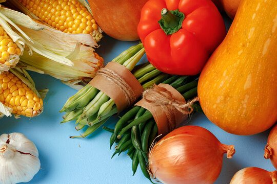 Pile of vegetables including pumpkin, onion and pepper on blue background