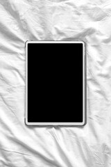 Top view mockup image of blank screen tablet on white bed sheets. Vertical orientation